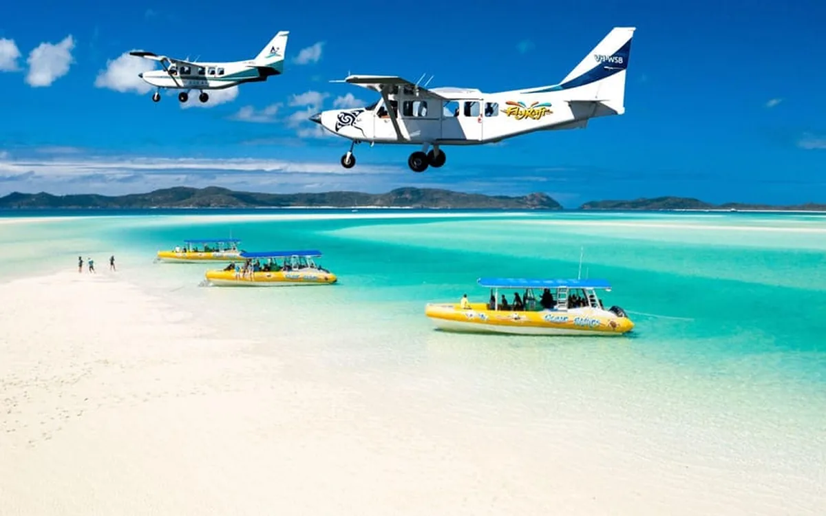 Una avioneta sobrevolando Whitehaven Beach con una lancha neumática en las aguas someras